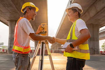 Asian civil engineer and surveyor engineers happily shake hands after work  at road construction...