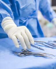 Hand of doctor or surgeon in blue gown pick up surgical clamp instrument or tools inside operating...