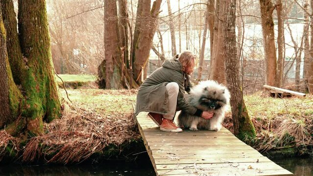A blond young man and a very fluffy and cute gray wolf spitz. The man strokes his friend but this seems to resist a bit here, but the man can not hold back his love probably.