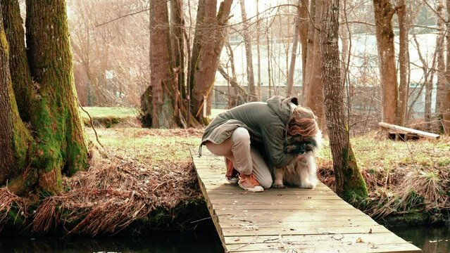 Very very cute how the young blonde man cuddles his dog. The gray and very fluffy wolf spitz looks around a bit and then takes a few steps on the bridge they are sitting on.