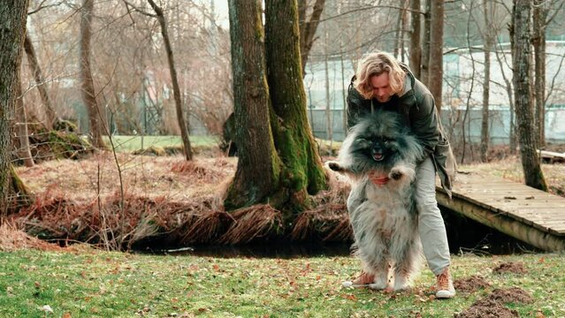 A man and his dog. Here a young blond man and his gray and very fluffy wolf dog are in an autumnal landscape and walk together a few steps while the man holds the dog.