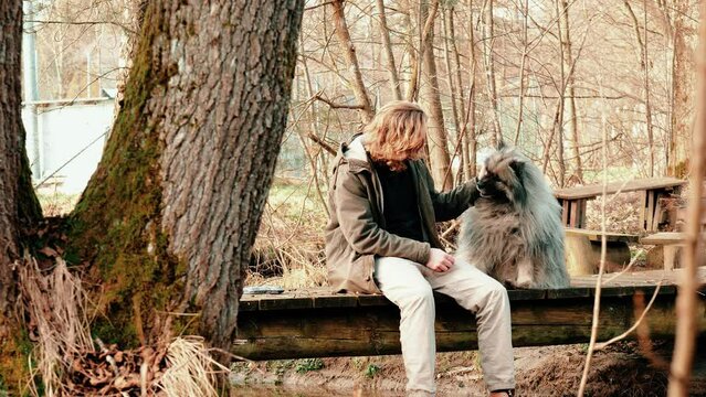 Two best friends on a small bridge. The young blond man heartily strokes his best friend, a gray and fluffy wolf Spitz. A breathtaking autumnal ambience gives this video a special flair.