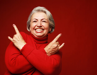 Portrait of funny senior gray-haired woman wearing red sweater and glasses doing a rock and roll symbol