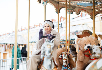 Pretty woman saddled a horse on a carousel.