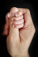 A newborn baby after birth clings tightly to the finger of the parents. Close-up of a small hand of a child and the palm of a mother and father. The concept of education, child care and healthcare.