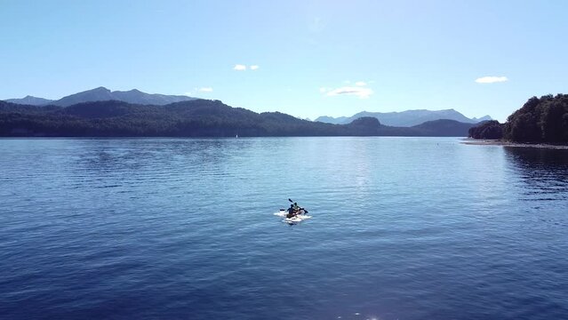 Aerial static shot of a Kayak with two people in the lake of Nahuel Huapi in Patagonia Argentina with Andes mountain range in the background.