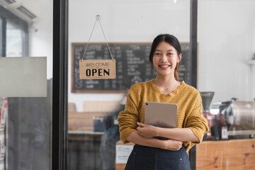 Young woman is a waitress in an apron, the owner of the cafe stands at the door with a sign Open waiting for customers. Small business concept, cafes and restaurants