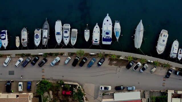 The aerial view of a yacht berth from the top showcases a colorful and organized arrangement of yachts and sailboats, each with their unique features, in a picturesque marina. Top view