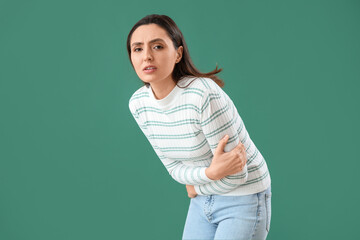 Young woman with abdominal pain on green background