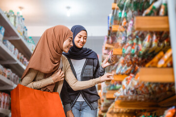 Two Muslim girls pick up a item on a shelf in a supermarket