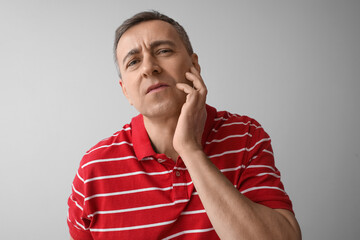 Tired mature man in red t-shirt on grey background, closeup