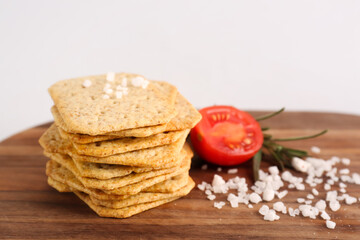 Board with tasty crackers, tomato, salt and rosemary on grey background