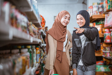 two happy muslim girls with pointing fingers while choosing shopping items in supermarket