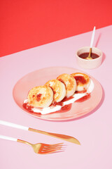 Plate of tasty cottage cheese pancakes with raspberry jam and sour cream on pink table