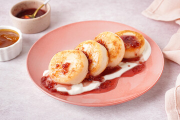 Obraz na płótnie Canvas Plate with tasty cottage cheese pancakes, sour cream and raspberry jam on light background