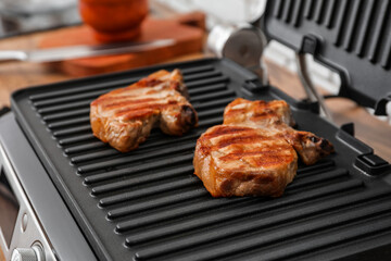 Modern electric grill with tasty steaks on table, closeup