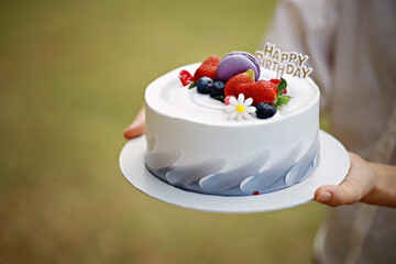 Female hand holding a beautiful fruits cake at outdoor park