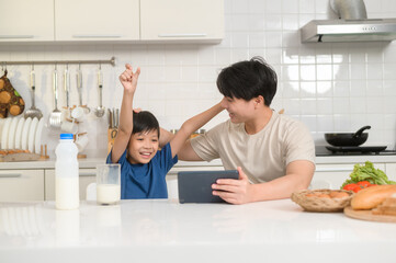 Young Asian father and his son using digital tablet enjoying together in kitchen at home