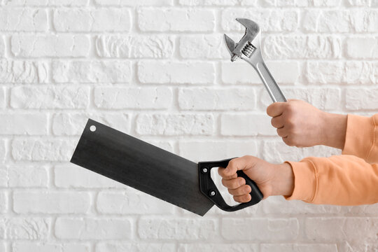 Worker with wrench and handsaw on white brick background