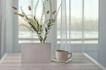 Template with photo frame or blank paper on a wooden table. Cup of coffee. Bouquet of Lagurus and dried branches. Sunlight from the window.	