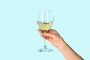 Female hand holding glass of white wine on blue background