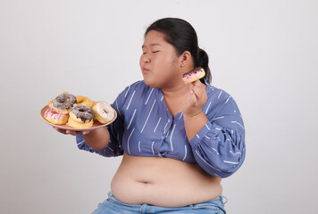 Happy fat woman eating donuts on plate isolated on color background. Food addiction, diet...