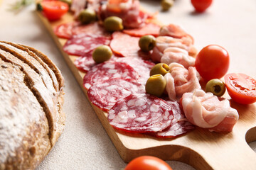 Wooden board with assortment of tasty deli meats on light background, closeup