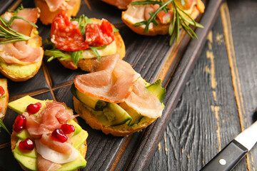 Board of tasty bruschettas with ham on dark wooden background, closeup
