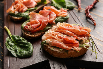 Boards of tasty bruschettas with ham on dark wooden background, closeup