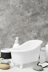 Naklejka na ściany i meble Small bathtub, spa stones, cosmetic products and cotton pads on table