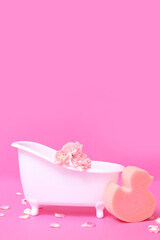 Small bathtub with carnation flowers and sponge on color background