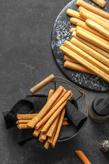 Slate board and basket with tasty Italian Grissini on dark background