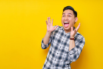 Handsome young Asian man surprised in plaid shirt looks aside and spreads his hands say wow...