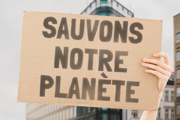 A person holding a brown save our planet cardboard poster. Carbon Footprint. Climate Change. Ecosystem. Biodiversity. Deforestation. Reforestation. Composting. Solar Energy. Wind Power. Zero Waste