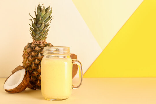 Mason jar of tasty pineapple smoothie and coconut on color background