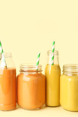 Glasses and bottles of different tasty smoothie with straws on yellow background