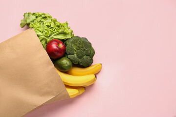 Paper bag with vegetables and fruits on pink background
