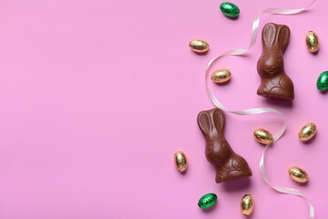 Chocolate bunnies, Easter eggs and ribbon on pink background