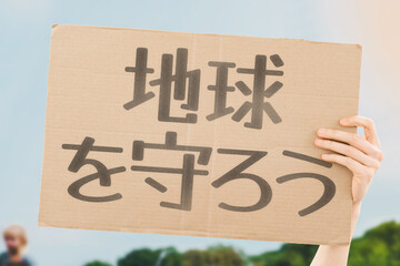 A person holding a brown save our planet cardboard poster. Carbon Footprint. Climate Change. Ecosystem. Biodiversity. Deforestation. Reforestation. Composting. Solar Energy. Wind Power. Zero Waste