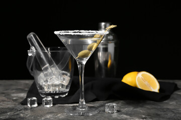 Glass of tasty martini with olives, ice cubes and lemon on dark background