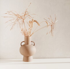 Dry grass branches in a beige vase standing on a beige wall with copy space. Minimalistic stylish...