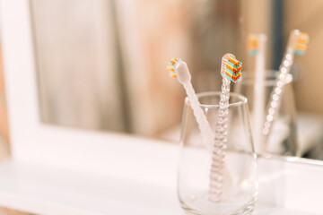 Children's toothbrushes in glass cup in front of mirror.
