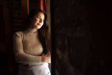 portrait of young woman looking pensively through the window in a brick room