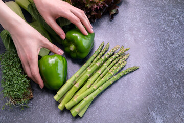 Someone Hands Hold Assortment Of Fresh Organic Home Grown Green Vegetables On Granite Table. Asparagus Plant, Bell Pepper, Bok Choy, Red Leaf Lettuce, Bittercresses. Bio food.Horizontal, copy space.