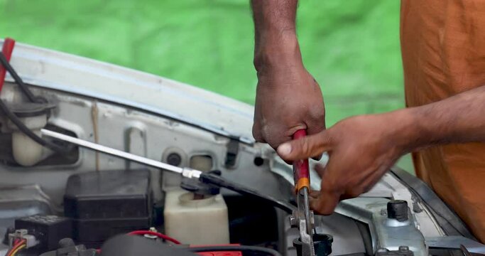 A man is fixing a car with pliers, or flat-nosed pliers, or wire cutters.