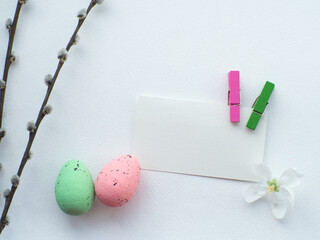 Happy Easter, white concept. Easter decorations on white background with copy space. Easter greating card. Flat lay. Apple tree twig, green and pink eggs and white flower. Celebrating Easter holidays.