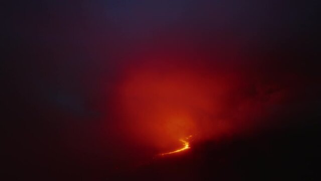Aerial above glowing at night magma and orange cloud above Mauna Loa mountain. Incredible dramatic volcanic eruption. Crazy flyover above lava river flowing from crater on Hawaii Island active volcano