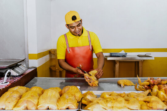 Latin man working as Poultry vendor of raw chickens being sliced by the Pollero at Chicken shop or Polleria in Mexican market in Mexico, Hispanic people