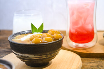 Bubur Sumsum Biji Salak or Candil Ubi served on wooden table, Indonesian traditional dessert porridge of rice flour, coconut milk with brown sugar syrup. Ramadhan iftar food
