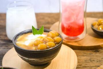 Bubur Sumsum Biji Salak or Candil Ubi served on wooden table, Indonesian traditional dessert porridge of rice flour, coconut milk with brown sugar syrup. Ramadhan iftar food